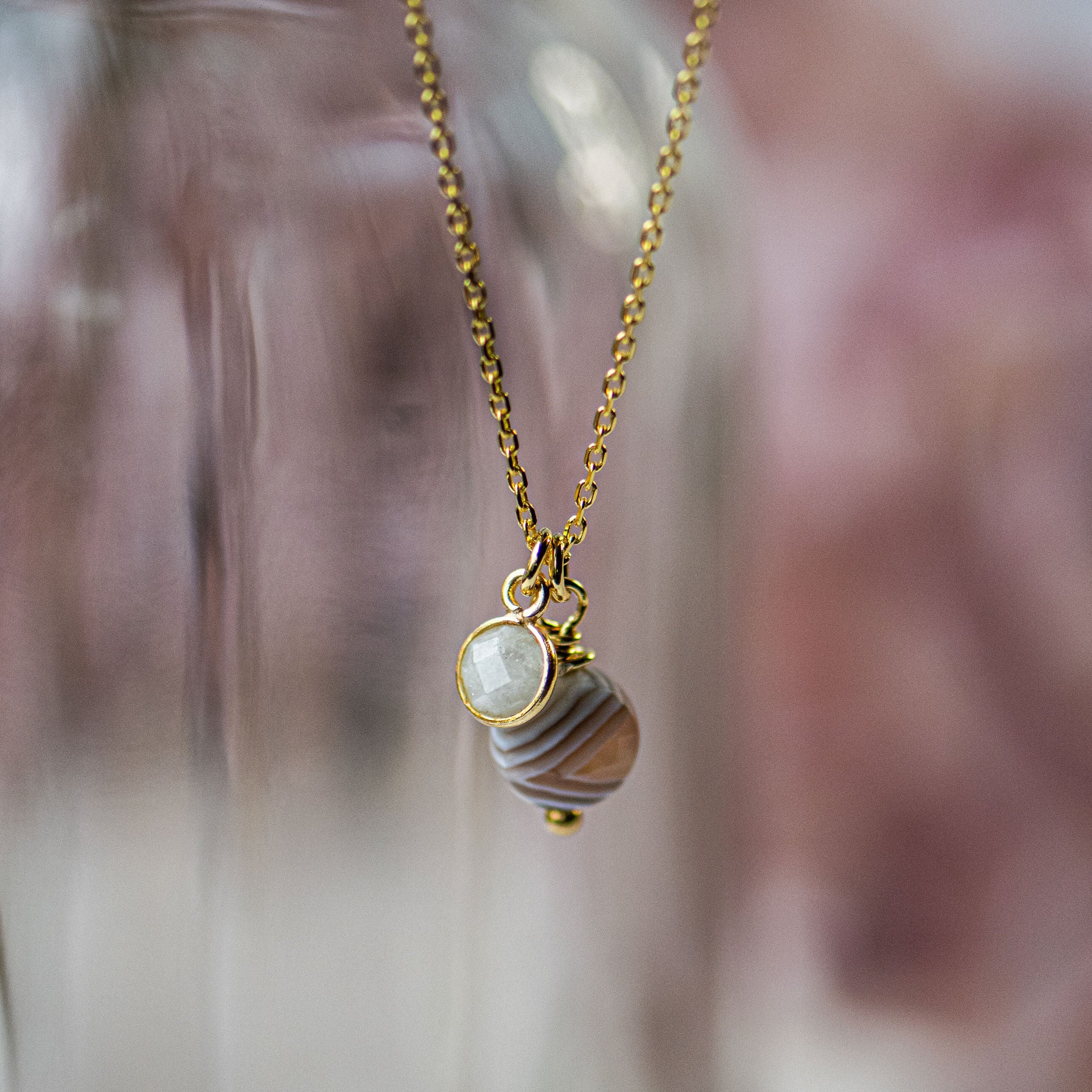 Gold necklace with a pendant featuring a pearl and brown stone against a blurred background